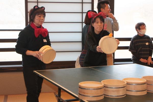 頭に猫の耳のようなものをつけた女性と赤色のリボンをつけた女性がおり、リボンをつけた女性が卓球玉を打ち返している写真